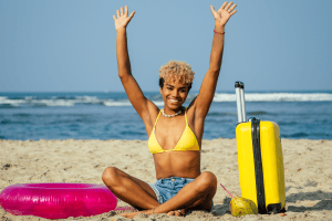 Jeune femme en biquini jaune à la plage avec valise jaune et bouée rose