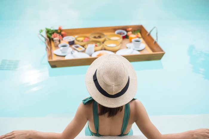 Jeune femme avec chapeau prenant petit déjeuner dans une piscine