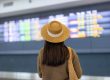 Femme brune aux cheveux longs avec chapeau ui regarde horaires sur le tableau d'affichage de l'aéroport.