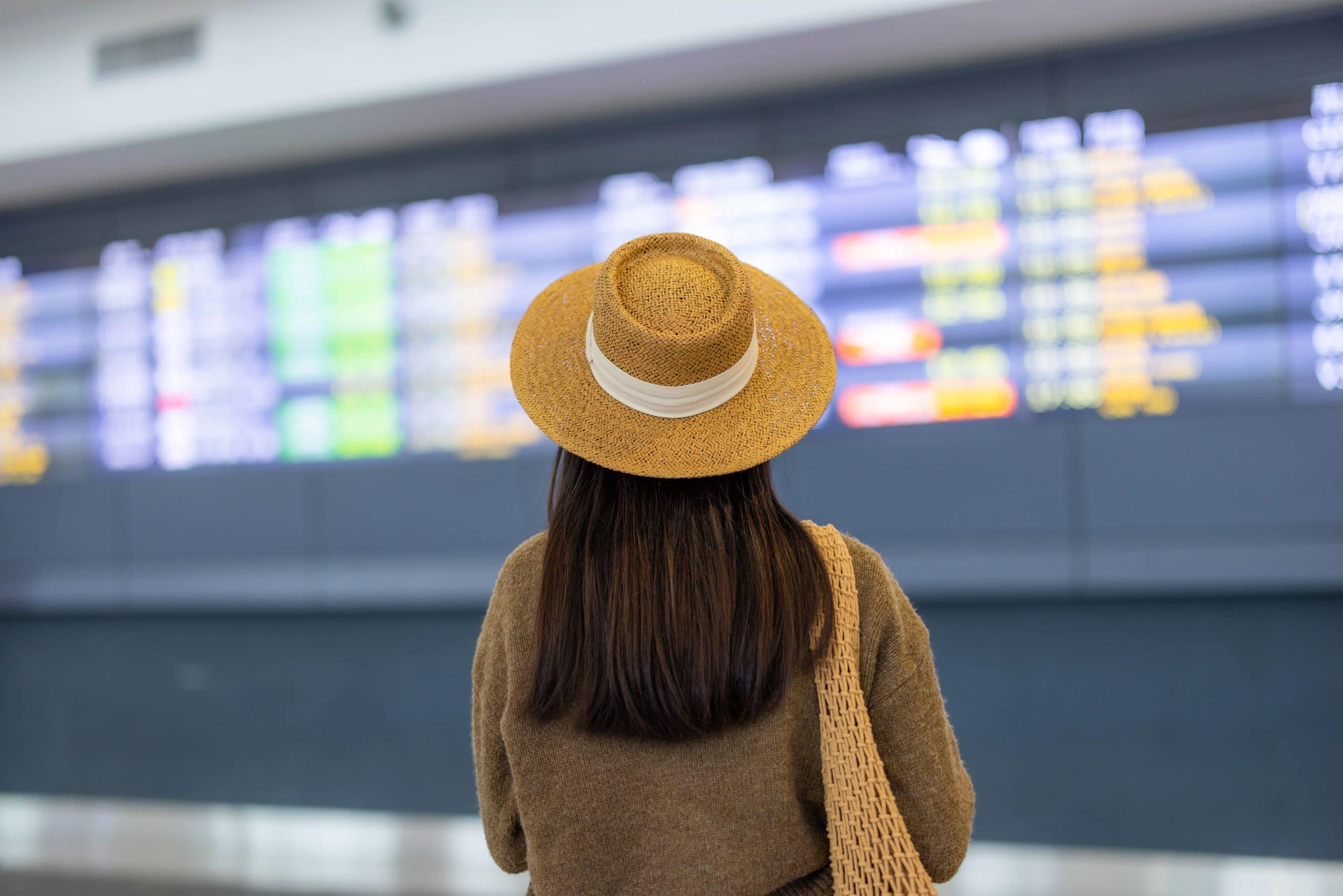 voyageuse qui regarde horaires de vol Femme brune aux cheveux longs avec chapeau ui regarde horaires sur le tableau d'affichage de l'aéroport.